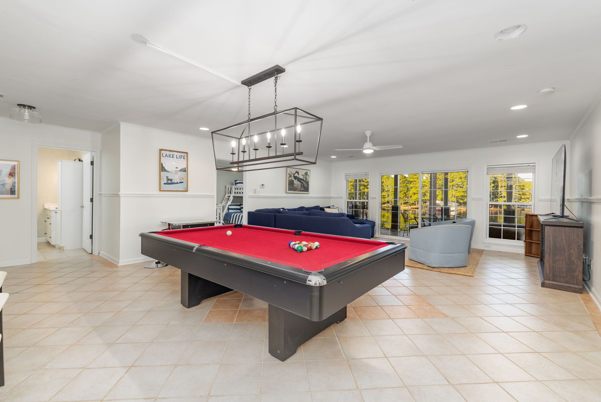 Een pooltafel in een ruime kamer met een plafondventilator, grote ramen en een blauwe bank.