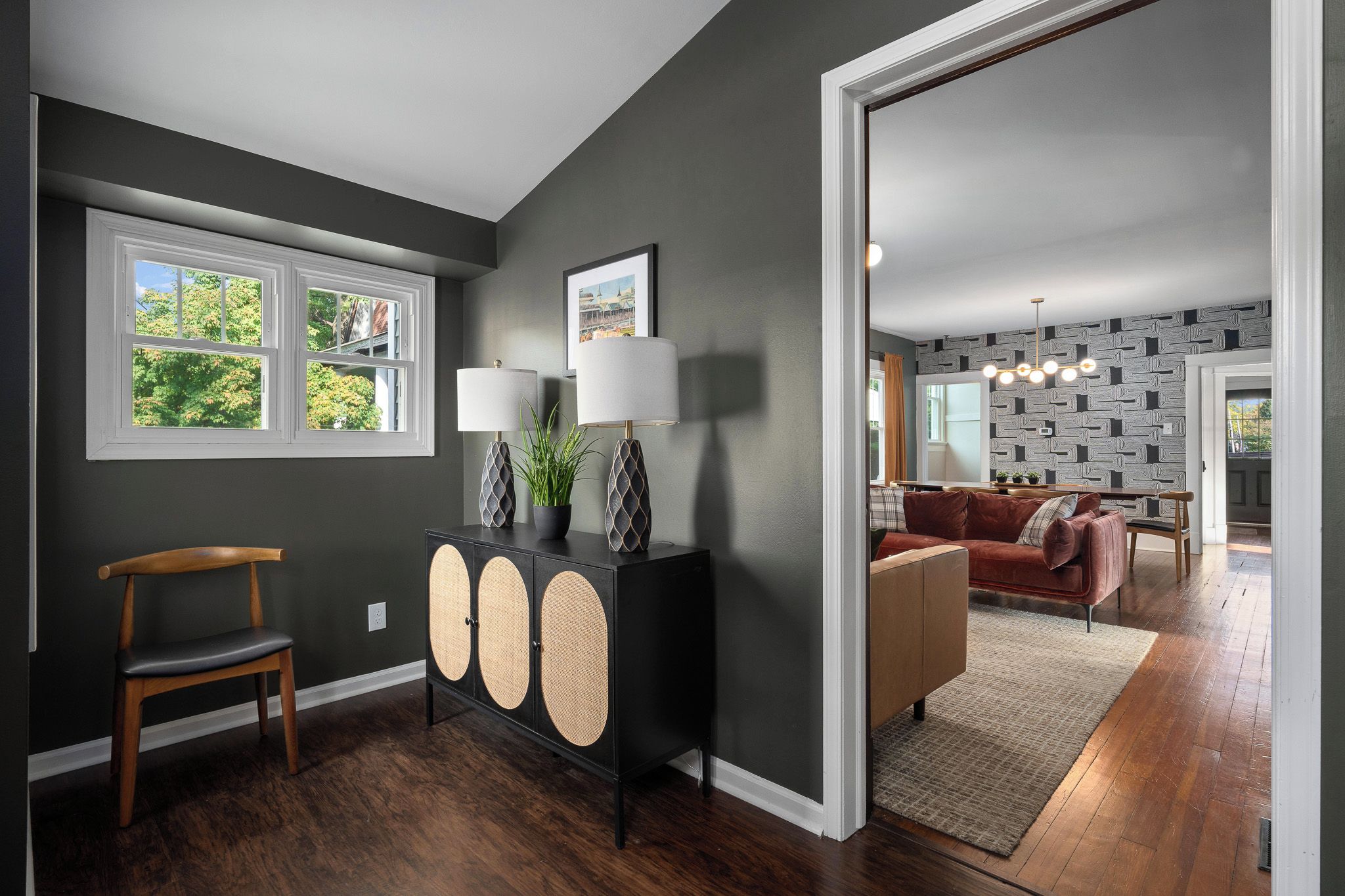 Un salon moderne avec un mur gris foncé, une chaise en bois, une console noire avec deux lampes et un canapé rouge.