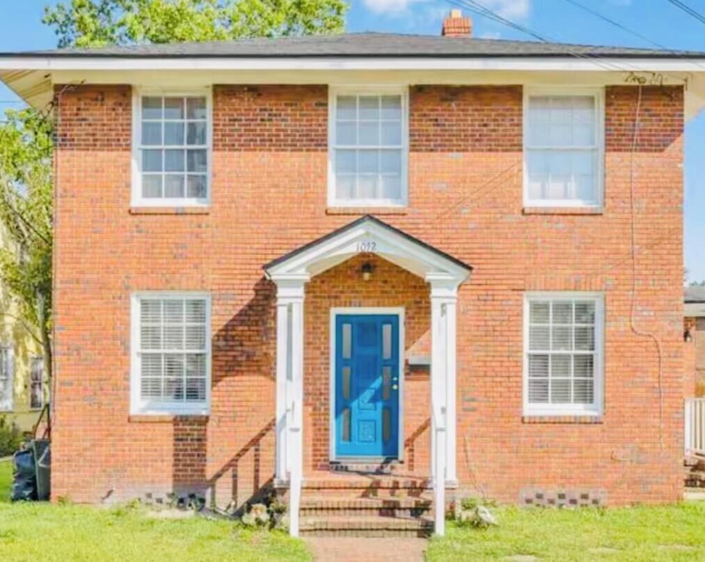 A two-story brick house with a blue front door, white window frames, and a small porch.