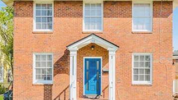 A two-story brick house with a blue front door, white window frames, and a small porch.