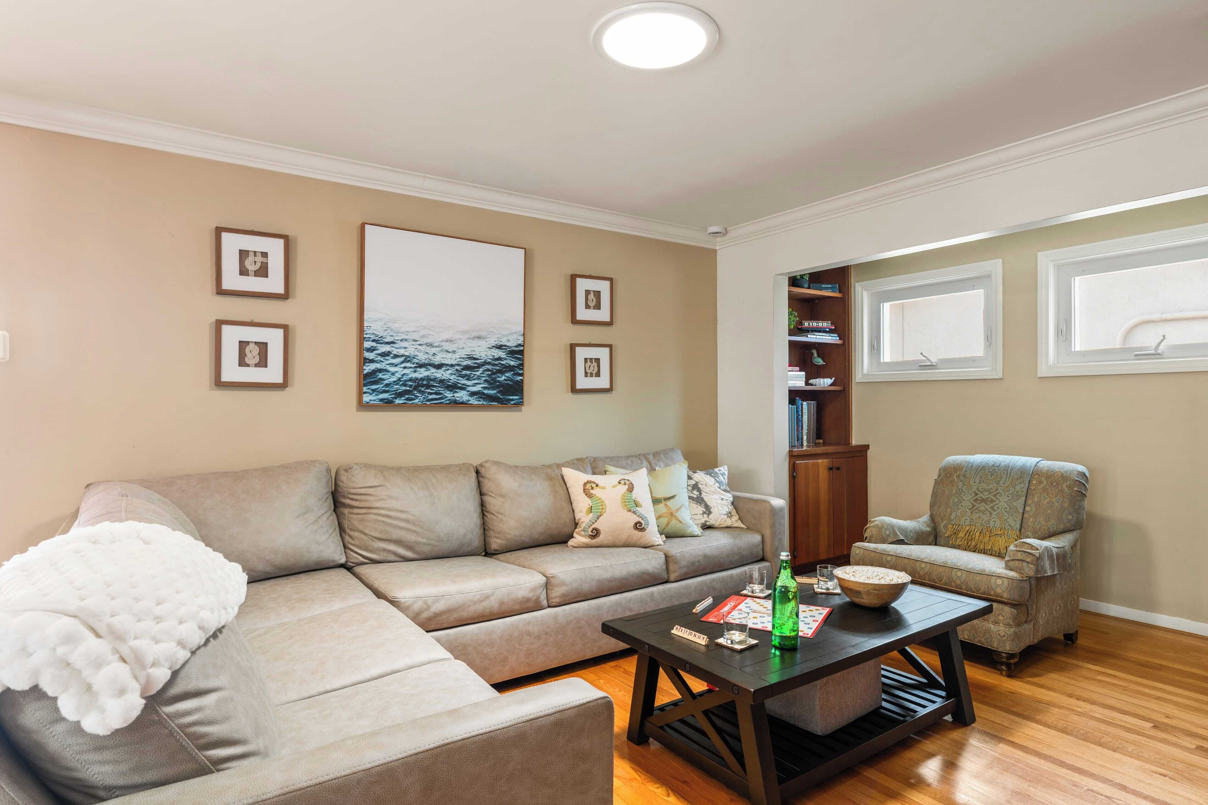 A living room with a beige sofa, a patterned armchair, a coffee table, and a bookshelf.