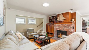 A cozy living room with a fireplace, a sofa, a coffee table, and a bookshelf. - Point Loma Home w/ Putting Green, Firepit + Game Room & Beach Access Zola Street by Avantstay (San Diego)