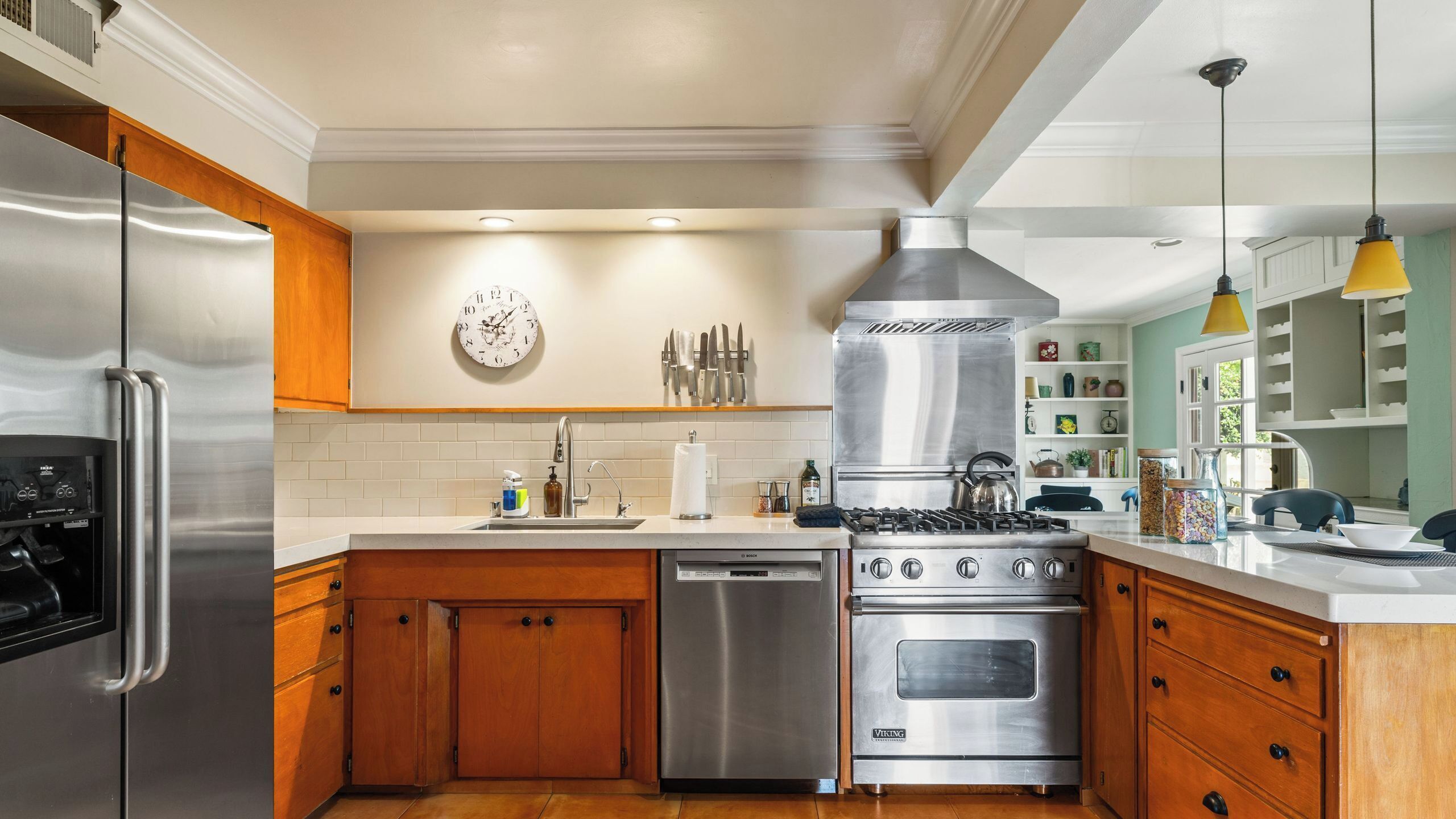A kitchen with stainless steel appliances, wooden cabinets, a dishwasher, a stove, and a clock on the wall.