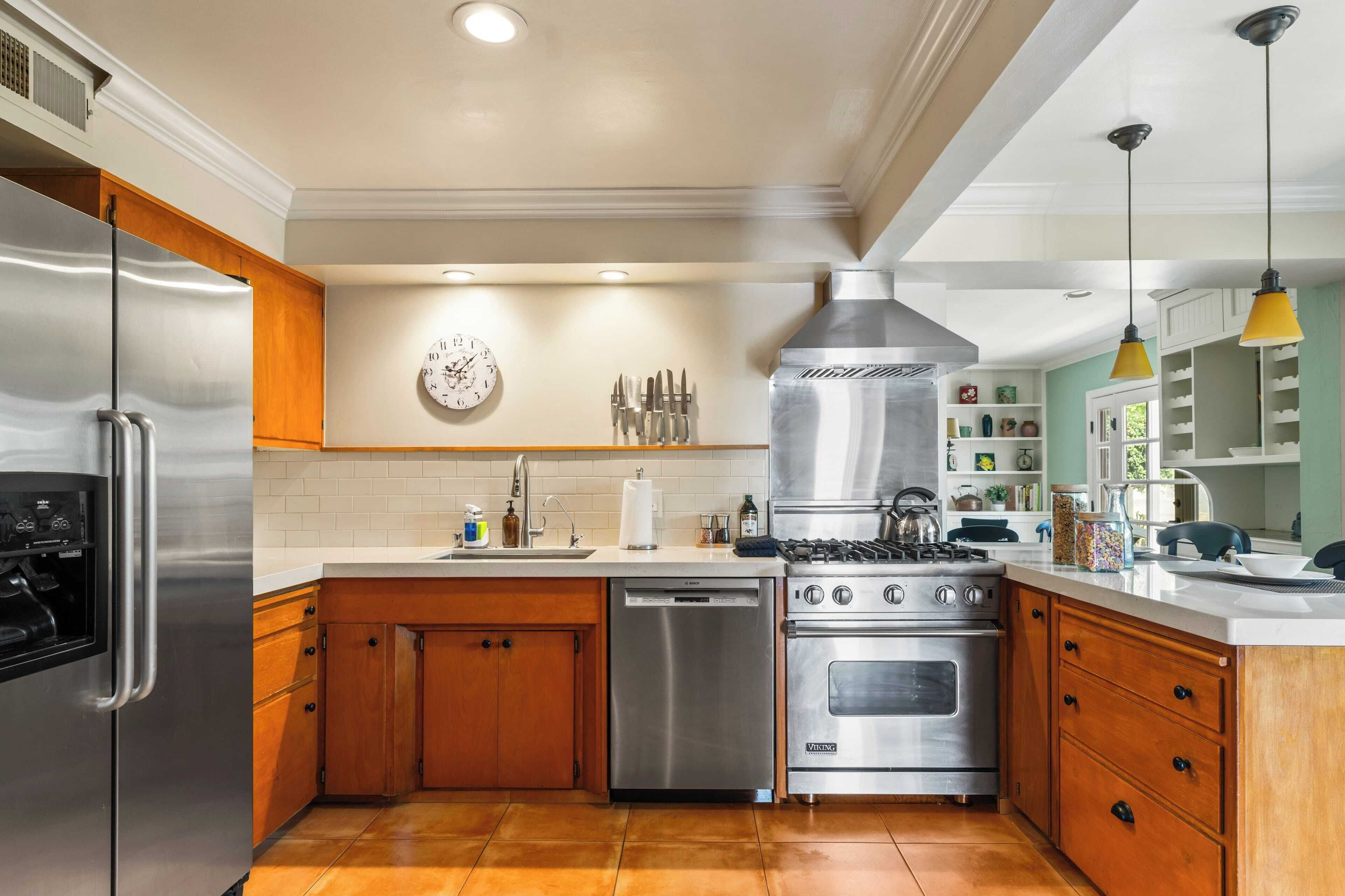 A kitchen with stainless steel appliances, wooden cabinets, a Bosch dishwasher, a Viking stove, and a clock on the wall.