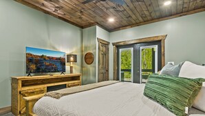 A bedroom with a wooden bed frame, a large window, and a painting on the wall.