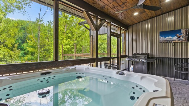 A hot tub with a view of a forest, a ceiling fan, and a painting on the wall.