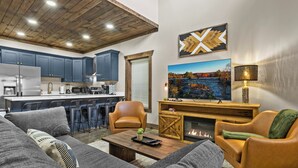 A modern living room with a sofa, chairs, a coffee table, a fireplace, and a kitchen in the background.