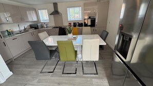 A modern kitchen with stainless steel appliances, a dining area with a white table and chairs, and a large refrigerator. - Modern Detached 4BR House – Super-King En-suite, Garden, Parking, Driveway (Sturry)