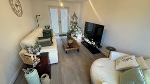 A living room with a white sofa, a coffee table, a TV, and a Christmas tree. - Modern Detached 4BR House – Super-King En-suite, Garden, Parking, Driveway (Sturry)