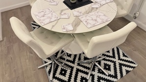 A round dining table with white chairs, marble placemats, and a small potted plant. - Modern Detached 4BR House – Super-King En-suite, Garden, Parking, Driveway (Sturry)