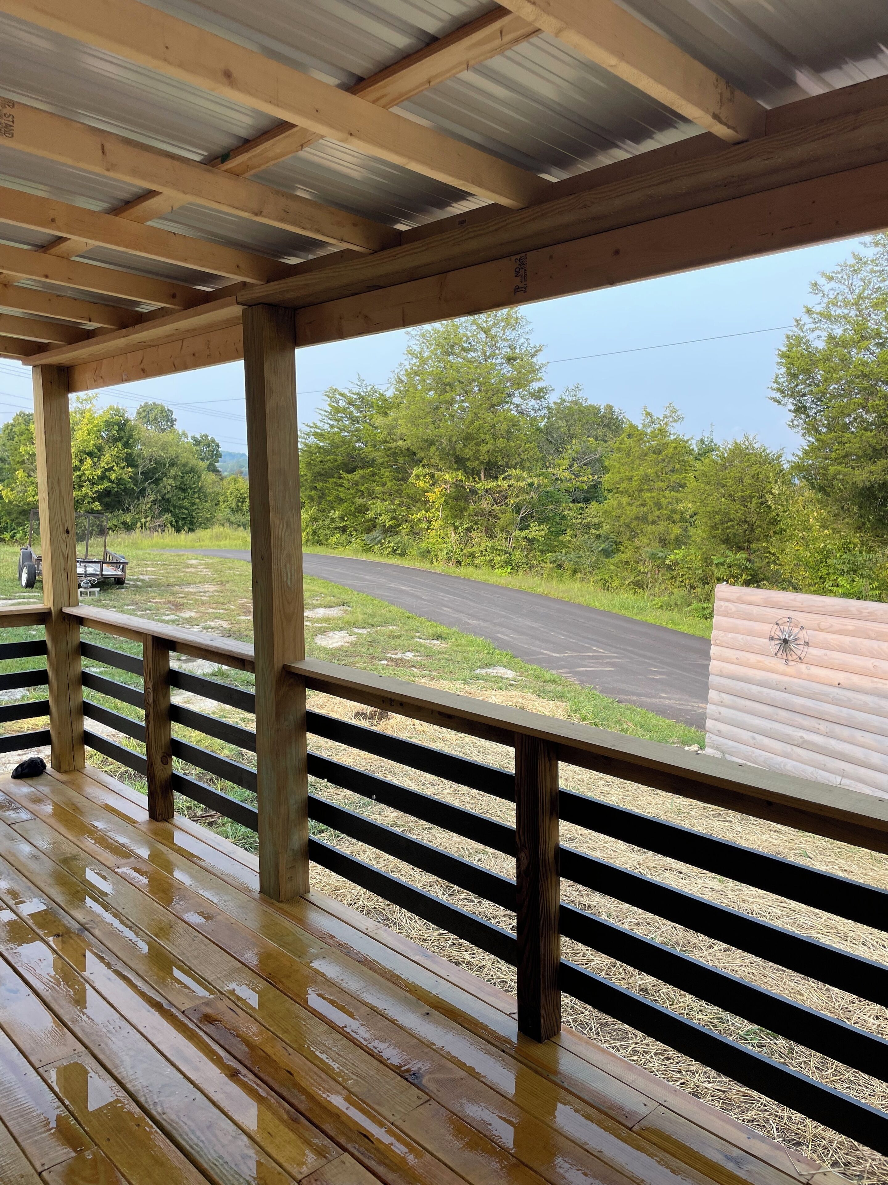 A covered wooden deck with a view of a road and greenery.