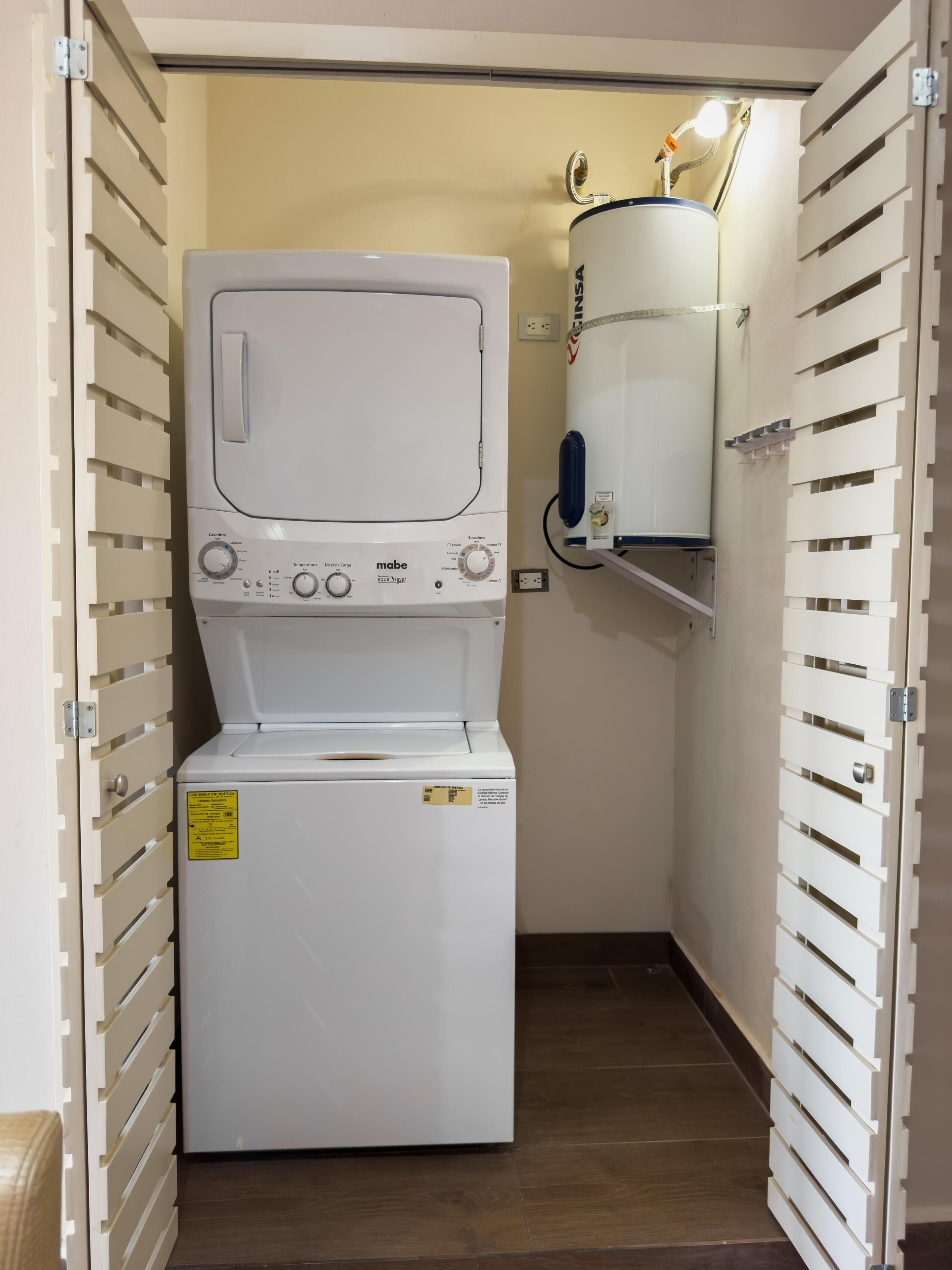 A compact laundry room with a front-loading washer and dryer, a water heater, and a wall-mounted shelf.