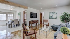 A spacious living room with a wooden ceiling, a flat-screen TV, a sofa, a coffee table, and a dining area with a table and chairs.