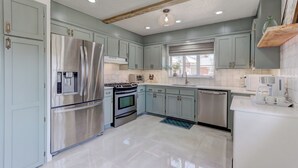 A modern kitchen with light blue cabinets, stainless steel appliances, and a wooden ceiling beam.