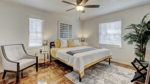 A bedroom with a bed, a chair, a ceiling fan, and a potted plant.