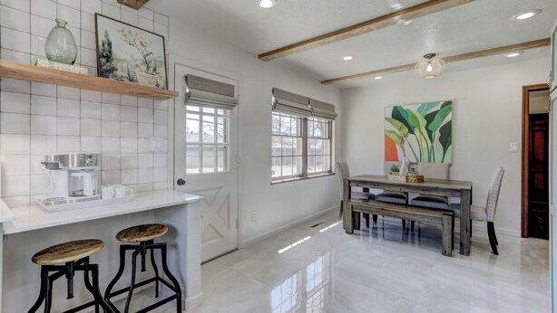 A kitchen with white tiles, a wooden bar counter, two stools, and a dining table with chairs.