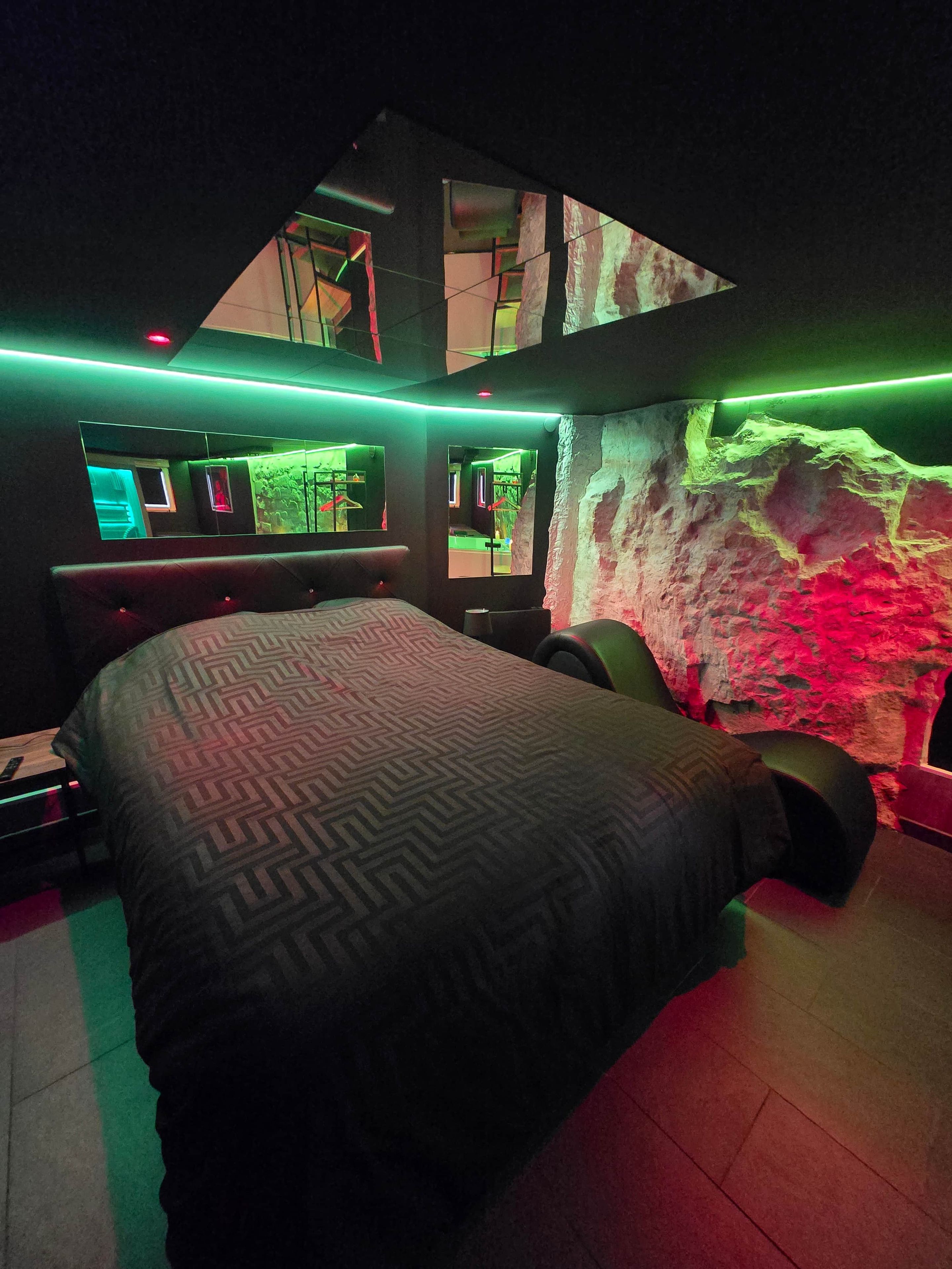 A modern bedroom with a large bed, a mirror, and a unique rock wall.