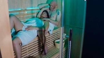 Een sauna met twee personen die op aparte banken liggen, een houten interieur en een glazen omheining.