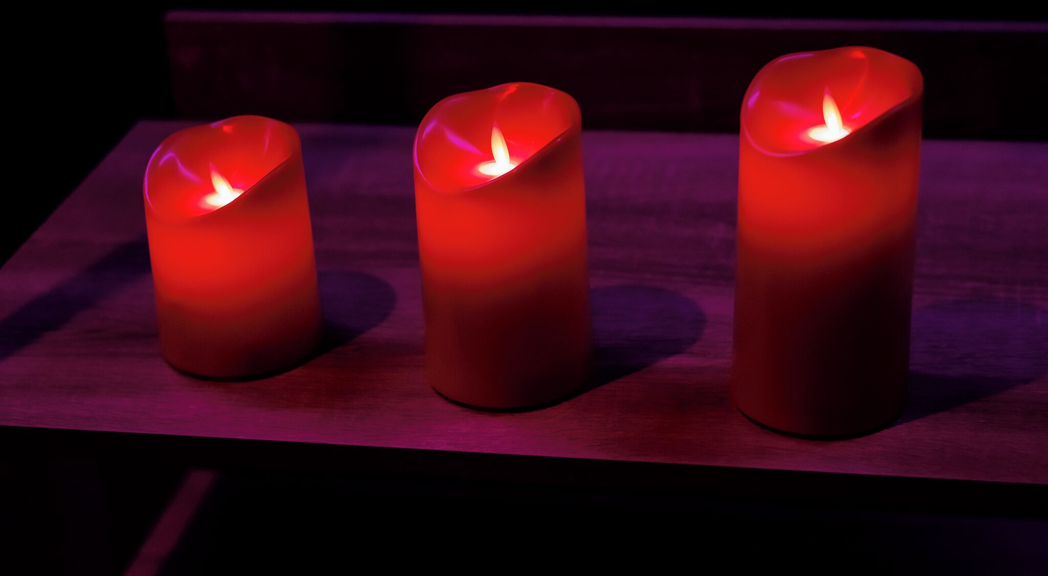 Three red candles on a wooden surface.