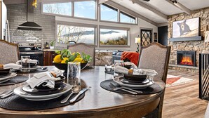 A dining area with a large table set for a meal, a stone fireplace, and a scenic view through the windows.