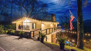 A cozy lodge with a stone chimney, a wooden deck, and string lights.