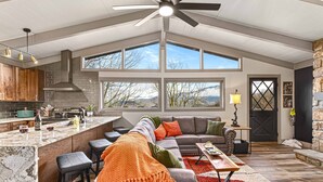 A spacious living area with a large window, a fireplace, and a kitchen with a high ceiling and modern appliances.