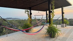 A hammock under a wooden pergola with a view of the sea and hills.