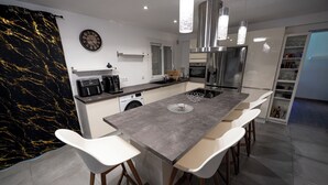 A modern kitchen with a central island, white bar stools, stainless steel appliances, and pendant lighting.