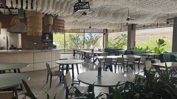 Un ristorante con tavoli e sedie rotonde, un'area bar e ampie finestre che offrono vista sul verde.