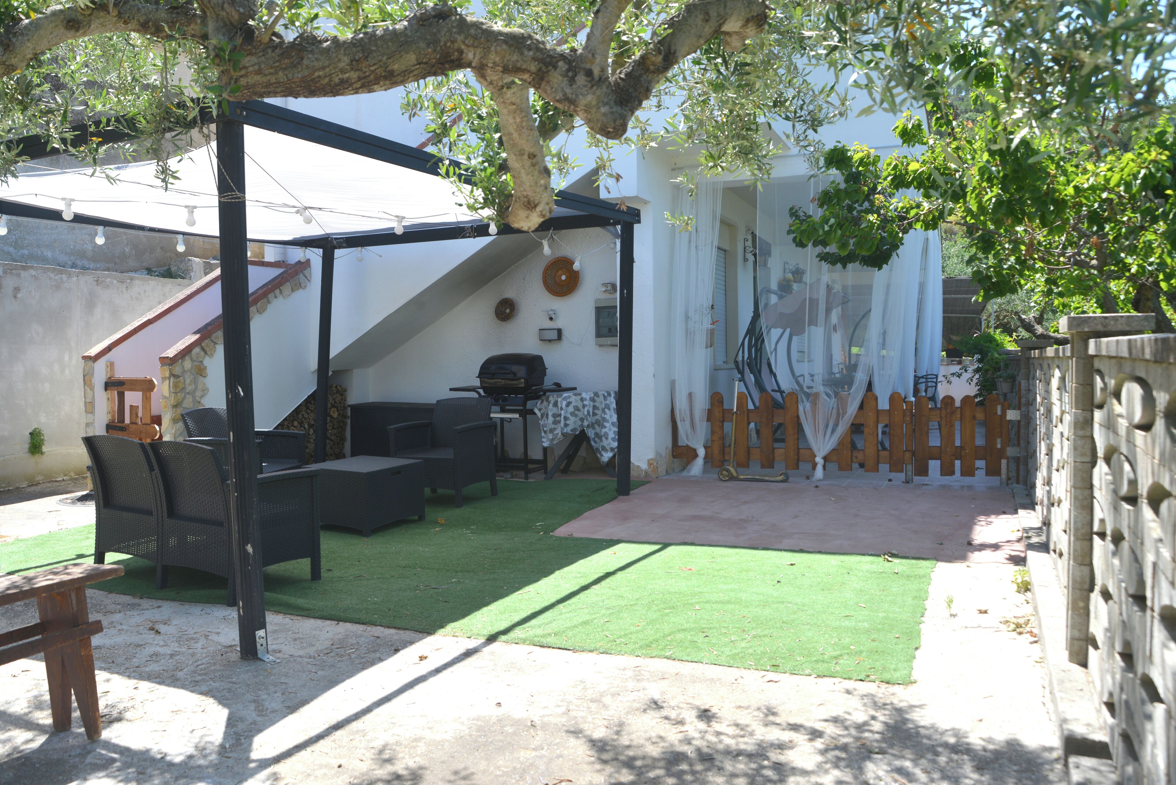 A covered outdoor seating area with a grill, artificial grass, and a wooden fence.