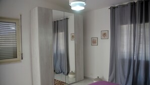 Une chambre à coucher comprenant un lit, une armoire, un miroir, une fenêtre avec des stores et un luminaire au plafond.