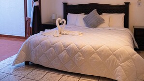 A hotel room with a large bed, a nightstand, a wall-mounted light, and a view through a window with curtains. - Hotel Casa Linda (San Cristobal de las Casas)