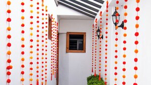 A narrow corridor with white walls, tiled floor, and red and orange hanging decorations. - Hotel Casa Linda (San Cristobal de las Casas)