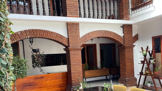 A multi-level outdoor patio with brick flooring, a glass-top table with yellow chairs, and potted plants. - Hotel Casa Linda (San Cristobal de las Casas)