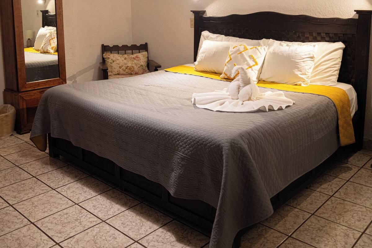 A neatly made bed with a gray and yellow bedspread, a wooden headboard, and a mirror on the wall.