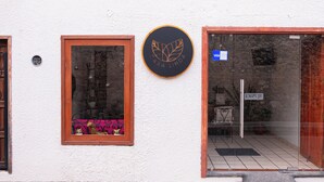 A building with a wooden door, a window with a metal grill, and a sign with a logo. - Hotel Casa Linda (San Cristobal de las Casas)