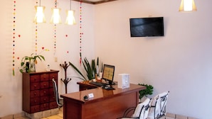 A room with a wooden desk, two chairs, a TV mounted on the wall, and hanging pendant lights. - Hotel Casa Linda (San Cristobal de las Casas)