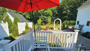 A wooden deck with a patterned table and chairs, a red umbrella, and a white fence. - Islesboro Suite in the Inn at Starlight Lodge (Maine)