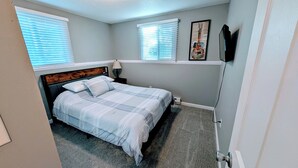 A bedroom with a bed, two windows, a wall-mounted TV, and a framed picture. - 2 Bed w/Garage Cardinal West Extended Stay (West Fargo)
