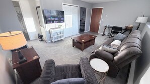 A living room with a sofa, armchair, coffee table, TV, and a lamp. - 2 Bed w/Garage Cardinal West Extended Stay (West Fargo)