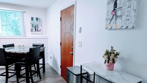 A modern, well-lit room with a dining table, chairs, a small desk, and a door. - 2 Bed w/Garage Cardinal West Extended Stay (West Fargo)