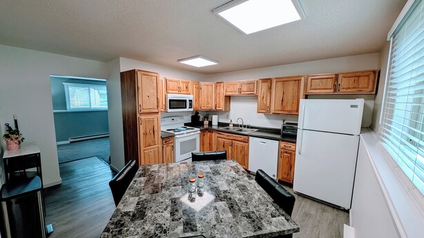 A compact kitchen with wooden cabinets, a granite countertop, and a white refrigerator. - 2 Bed w/Garage Cardinal West Extended Stay (West Fargo)