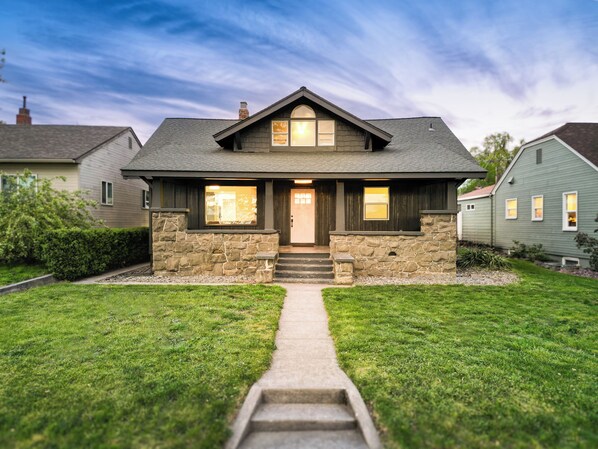 A two-story house with a stone facade, a front porch, and a pathway leading to the entrance.