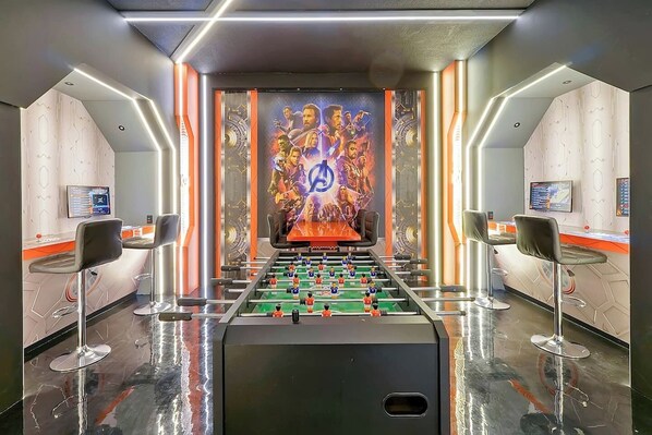 A room with a foosball table, two bar stools, and a large mural on the wall.