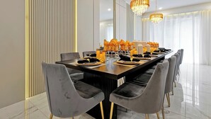 Een moderne eetruimte met een lange tafel, grijs beklede stoelen en decoratieve verlichting.