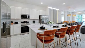 Een moderne keuken met witte kasten, roestvrijstalen apparatuur, een marmeren eiland en een bar met oranje stoelen.