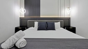 Een moderne hotelkamer met een groot bed, twee nachtkastjes, een hoofdbord met verticale lijnen en twee hanglampen.