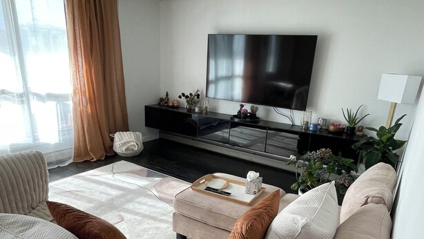 Ein modernes Wohnzimmer mit einem beige farbenen Sofa, einem Couchtisch und einem Flachbildfernseher auf einem schwarzen Standfuß.