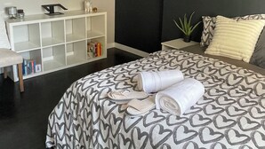Ein modernes Schlafzimmer mit einem großen Bett, einem weißen Konsolentisch, einem runden Spiegel und einer dunkel gestrichenen Wand.