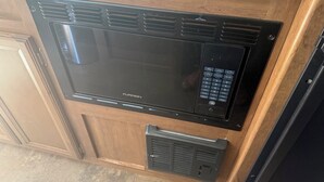 A black microwave oven with a digital control panel, installed in a kitchen with wooden cabinets and a granite countertop. - Cozy Vegas Bunkhouse RV (Las Vegas)